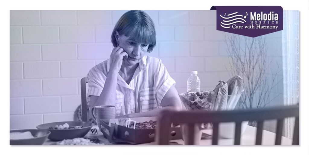 A sad elderly woman sitting alone on a chair in front of a dining table, showing signs of discontinuing her meal.