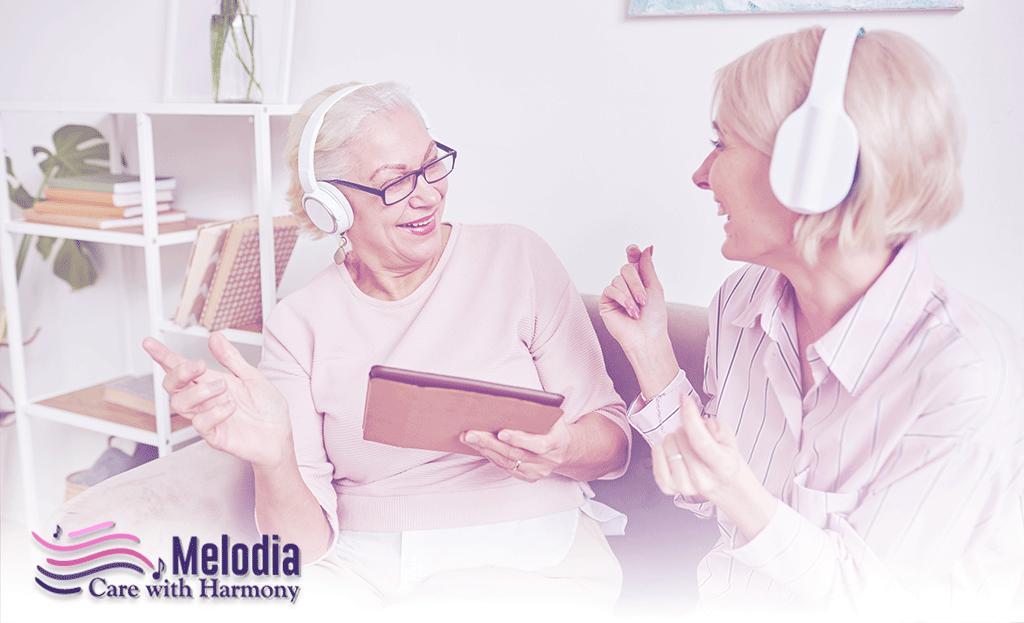 A hospice patient, an old lady, and her beautiful caregiver both wear headphones and enjoy music in a music therapy session. This image shows how music therapy can have a positive impact on hospice patients.