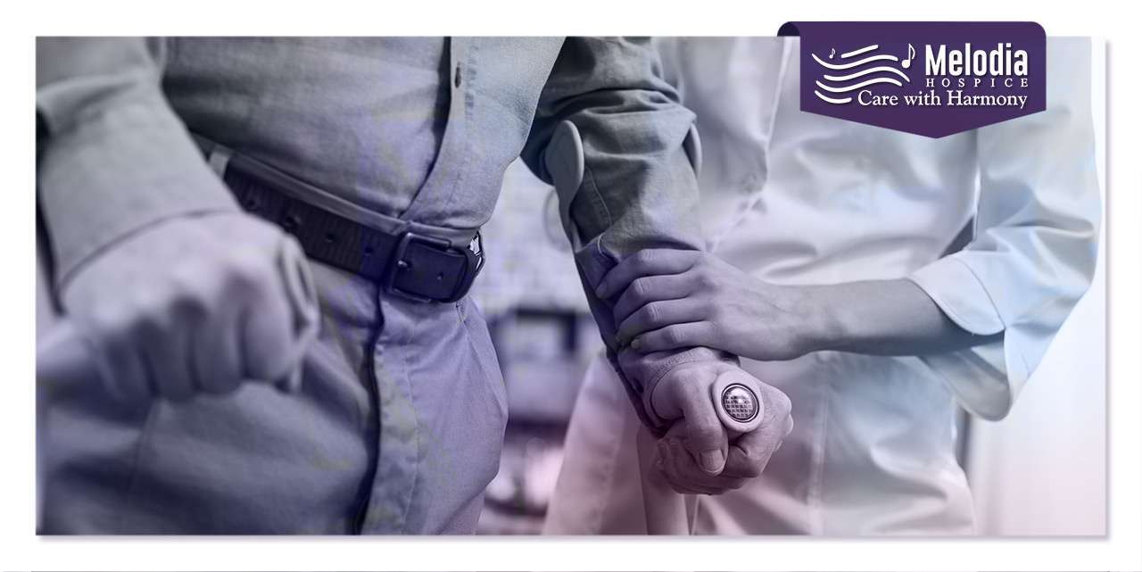 A patient standing with a support stick, accompanied by a female caregiver holding them, exploring if palliative care is the same as hospice.