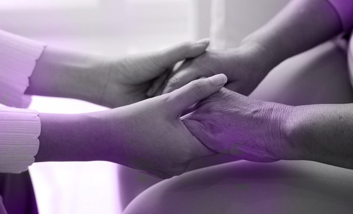 Young woman providing hospice care at home, holding the hand of an elderly woman